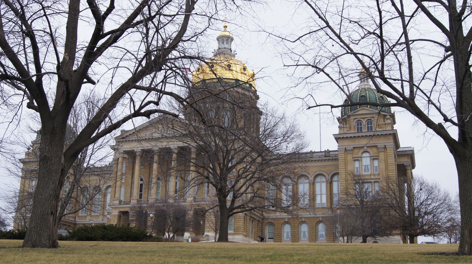 The Iowa State Capitol in Des Moines, with its gold dome, seen through bare winter trees